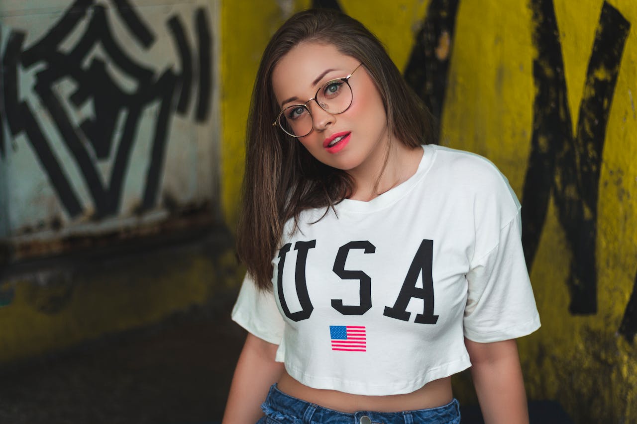 Stylish woman in a USA crop top posing with urban graffiti backdrop.