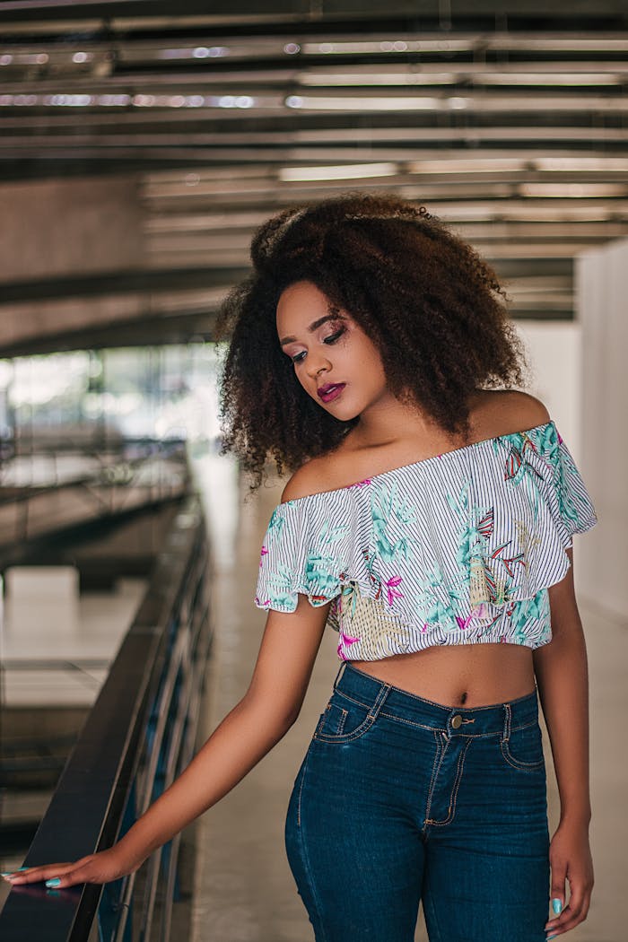Young woman in a crop top and jeans posing indoors with modern architecture.