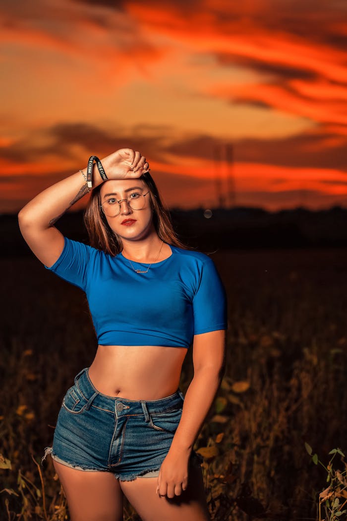 A woman in denim shorts poses confidently at sunset, creating a vibrant and bold scene.